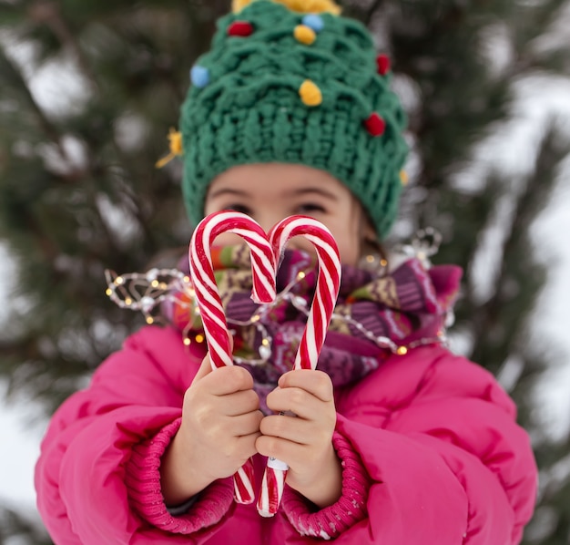 Happy child with a big candy canes under a christmas tree. Winter holidays concept.