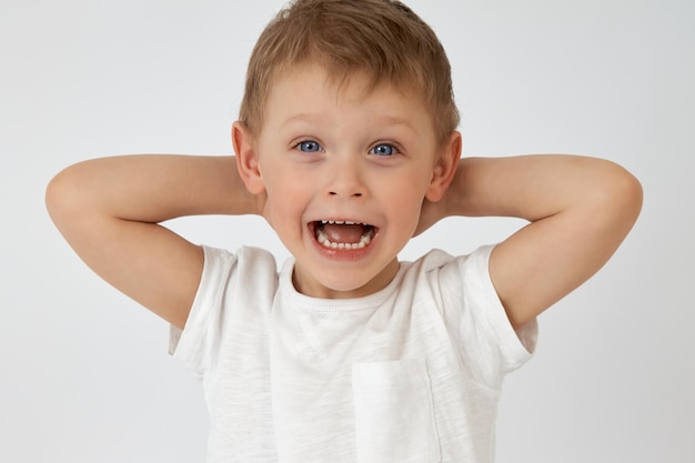 Happy child with blue eyes threw his hands behind his head on a white background