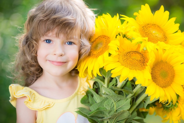 Happy child with bouquet of beautiful sunflowers against green background Spring family holiday concept Mothers day