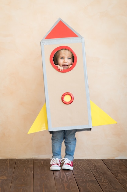 Happy child with cardboard rocket playing at home