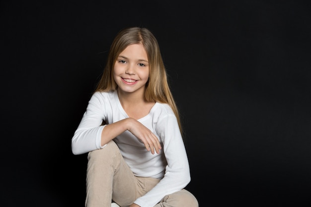 Happy child with fashion hairstyle on black background. Little girl smile with long blond hair. Beauty kid smiling with adorable look. Beauty salon. Keep calm and get your hair done.