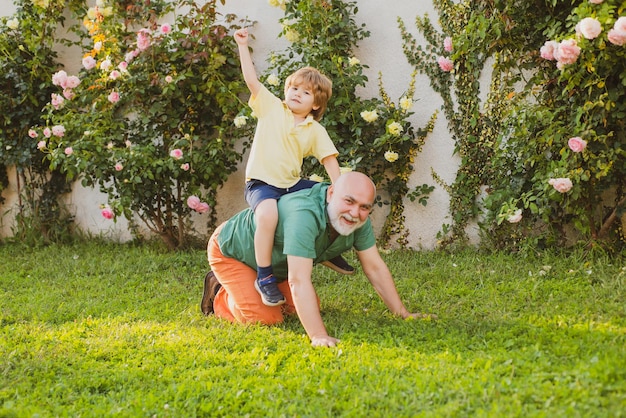 Happy child with grandfather playing outdoors father giving son ride on back in park grandfather wit...