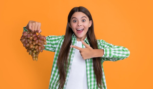 Happy child with grapes bunch on yellow background point finger diet