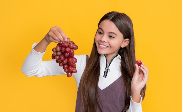 Happy child with grapes bunch on yellow background