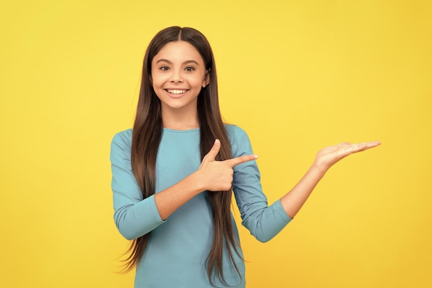 Happy child with long hair presenting product and point finger on copy space advertisement