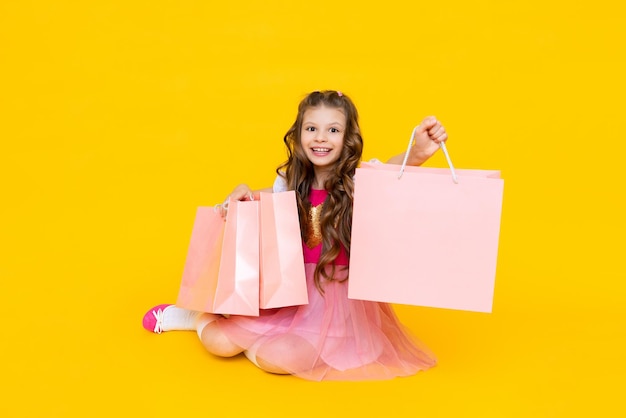 Photo happy child with packages after shopping the little girl is very happy about new purchases sale of children's clothing gifts for a little princess on a yellow isolated background