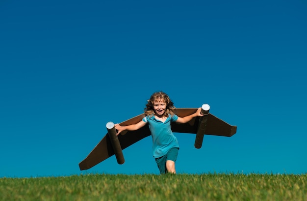 青い空に逆らって紙の翼を持った幸せな子供おもちゃのジェットパックを持った子供が春の緑のフィールドで楽しんでいます