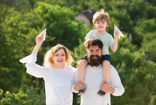 Happy child with parents playing with toy wings against summer sky background happy smiling boy on s