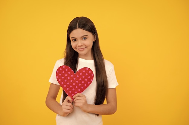 Happy child with red heart on yellow background with copy space charity