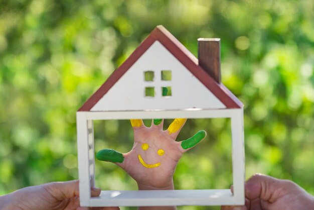 Foto bambino felice con il sorriso a portata di mano. famiglia che tiene casa in mano su sfondo verde primavera. concetto di ecologia ed immobile