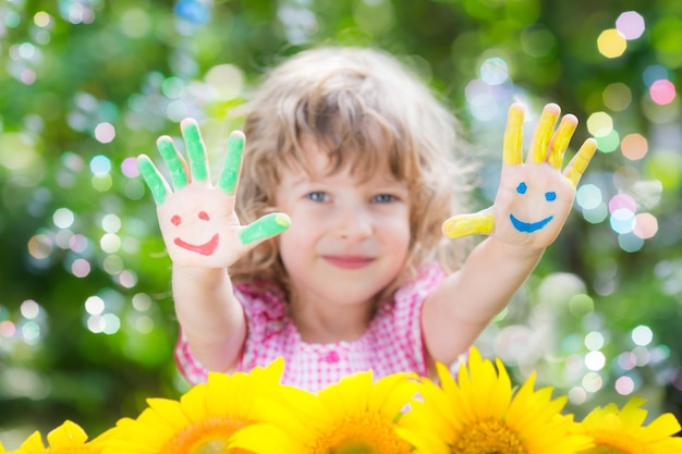 Happy child with smiley on hands against green spring background