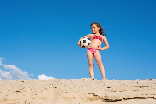 Happy child with a soccer ball on the beach on a sunny summer day