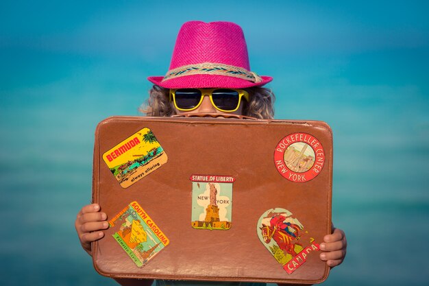 Счастливый ребенок с винтажным чемоданом на пляже
