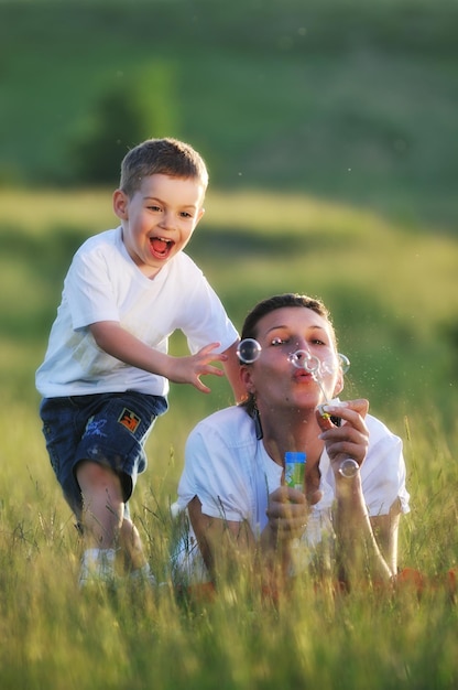 Foto bambino felice e donna all'aperto che giocano con la bolla di sapone sul prato