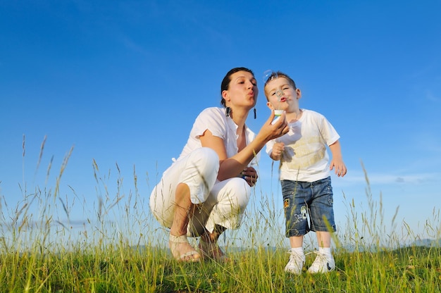 happy child and woman outdoor playing with soap bubble on meadow