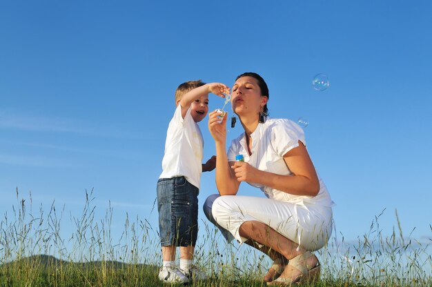Happy child and woman outdoor playing with soap bubble on meadow