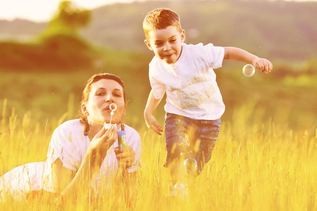 happy child and woman outdoor playing with soap bubble on meadow