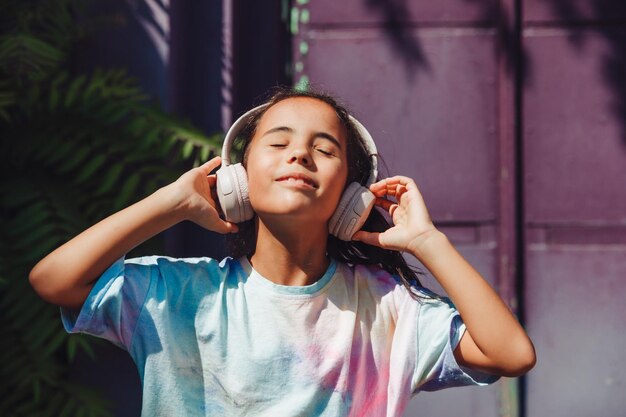Фото Счастливое детство счастливая маленькая девочка слушает музыку и танцует на улице маленький ребенок в наушниках весенняя и осенняя мода любимая музыка в наушниках поколение z