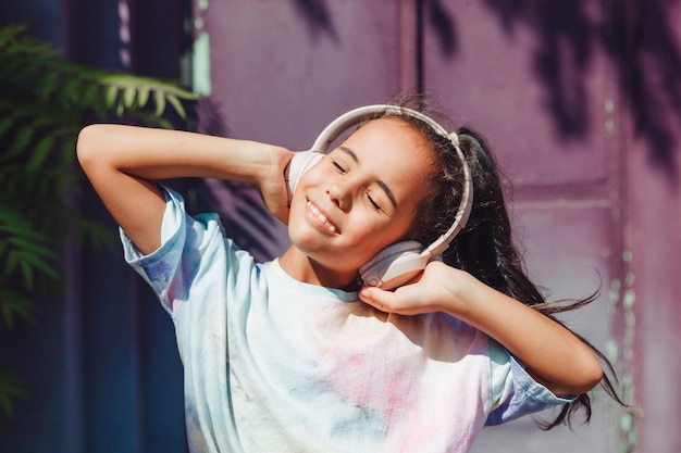 Фото Счастливое детство счастливая маленькая девочка слушает музыку и танцует на улице маленький ребенок в наушниках весенняя и осенняя мода любимая музыка в наушниках поколение z