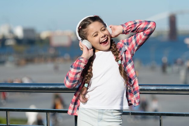 행복한 어린 시절 예쁜 소녀를 위한 헤드셋의 가을 분위기 행복한 어린 소녀가 음악을 듣습니다. 행복한 미소를 가진 작은 아이 봄과 가을 패션 헤드폰에서 좋아하는 음악 내 재생 목록이 최고입니다.