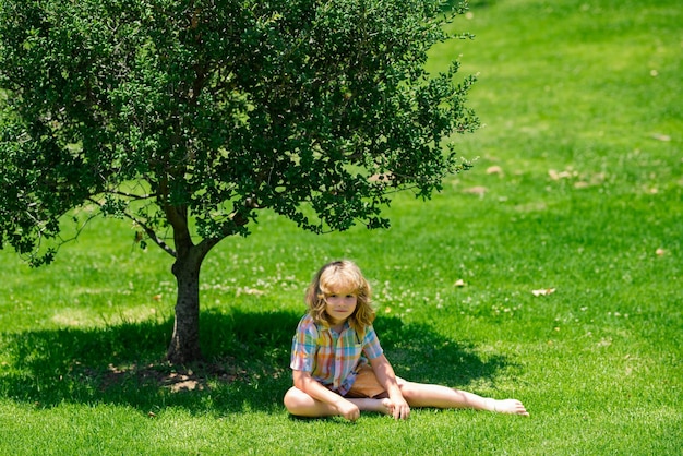 Happy childhood child relax at the summer park kid boy sitting on green grass outdoor summer picnic