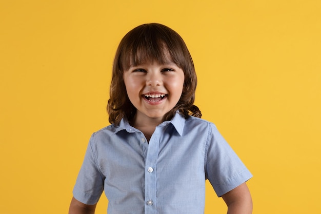 Happy childhood concept Adorable positive little boy laughing cheerfully looking to camera yellow studio background