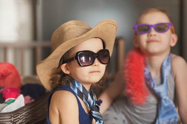 Happy childhood. Cute girl and boy playing in a fashion and wearing sunglasses, cowboy hat. Adorable childs having fun indoors.