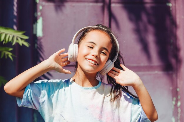 Happy childhood a happy little girl listens to music and dances\
in the street a small child wearing headphones spring and autumn\
fashion favorite music in headphones generation z