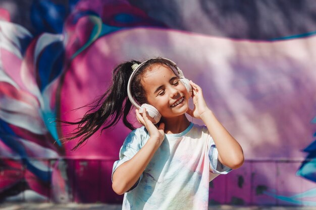 Happy childhood a happy little girl listens to music and dances\
in the street a small child wearing headphones spring and autumn\
fashion favorite music in headphones generation z