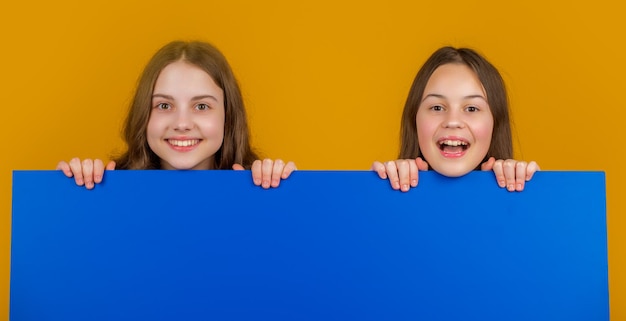 Photo happy children behind blank blue paper with copy space for advertisement on yellow background