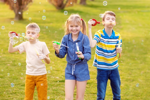 Happy children blow soap bubbles in the summer park.