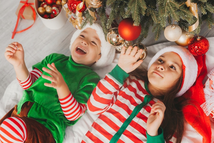 Photo happy children boy and girl lie on the floor near a festively decorated christmas tree. christmas