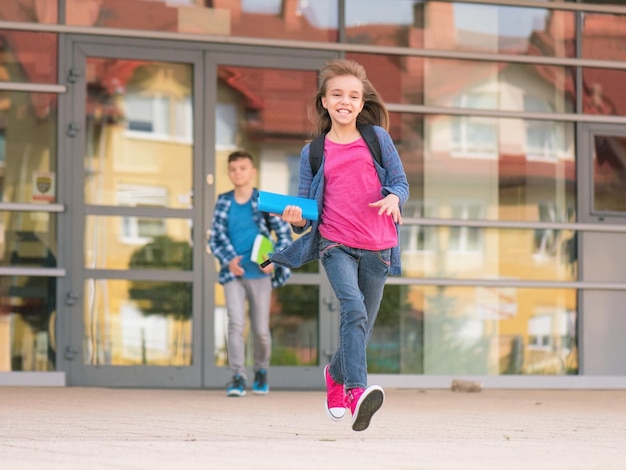 Happy children boy and girl with books and backpacks on the first school day Excited to be back to school after vacation Full length outdoor portrait