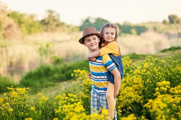 Happy children brother and sister, friends, outdoors in summer in a field of blooming yellow flowers