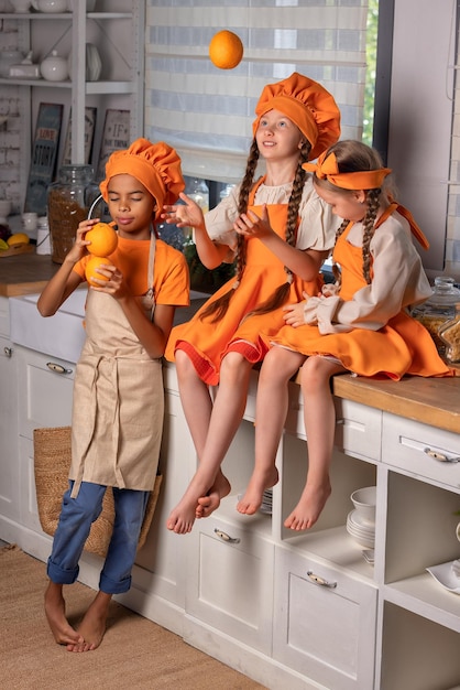 Happy children friends eating fresh orange and playing with fresh mandarin fruits in kitchen at home