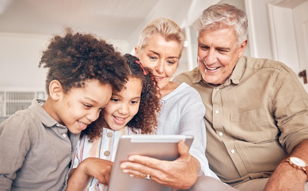 Happy children and grandparents with a tablet in a house streaming cartoon or a movie online App smile and interracial kids and senior man and woman with technology for a film game or website