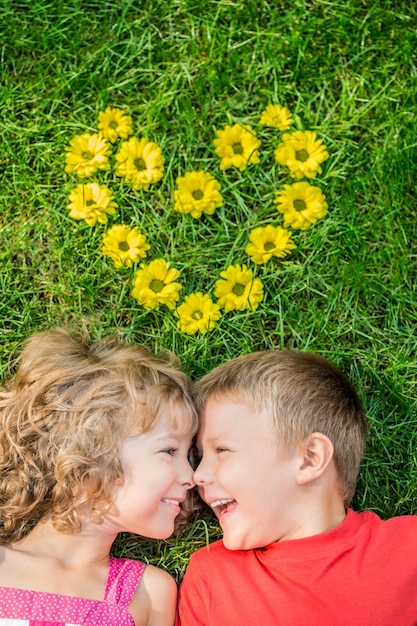 Happy children having fun outdoors Heart shape spring flowers Boy and girl lying on green grass Holiday concept Valentines day