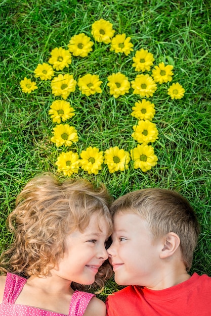 Happy children having fun outdoors House shape spring flowers Boy and girl lying on green grass Sweet home Renovation and moving concept