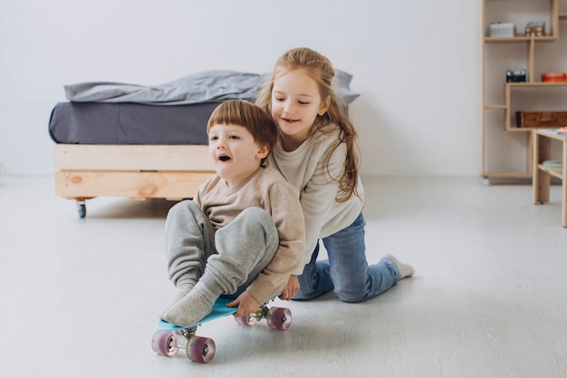 Bambini felici divertirsi con skateboard sul pavimento nella sala di casa.