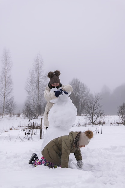 幸せな子供たちは田舎の雪に覆われた畑で雪だるまを作ります。