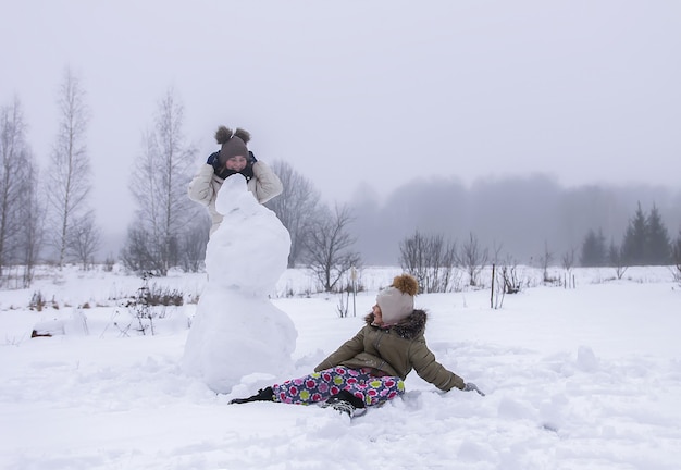 Happy children make a snowman in a snow-covered field in the countryside.