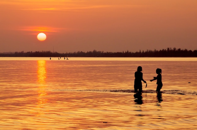 Bambini felici che giocano sulla spiaggia al tramonto