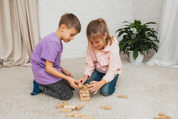 Счастливые дети сидят на полу и играют в образовательную игру (дженга) и стоят в башне из блоков