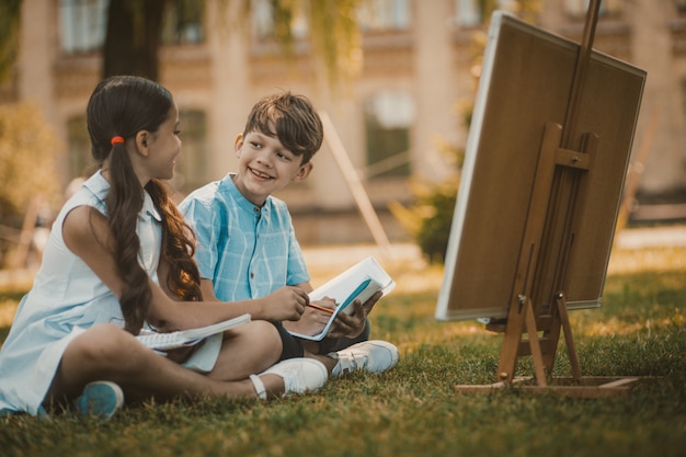 Happy Children Sitting At Green Grass In Park