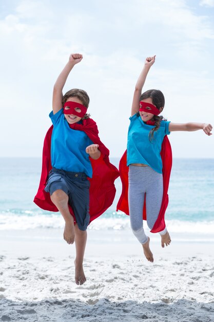 Happy children in superhero costume at beach 