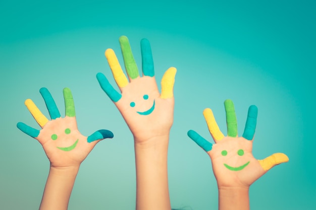 Happy children with smiley on hands against blue summer sky background