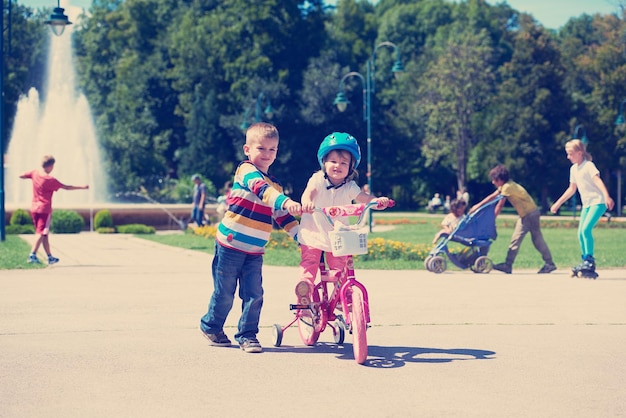 Счастливые дети на открытом воздухе, брат и сестра в парке веселятся. Мальчик и девочка в парке учатся кататься на велосипеде.