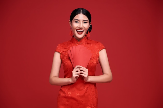 Happy Chinese new year. Asian woman wearing traditional cheongsam qipao dress holding angpao or red packet monetary gift isolated on red background.