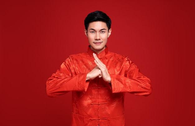 Счастливого китайского Нового года. Красивый азиатский мужчина жест поздравления на красный цвет.