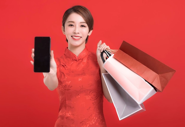 幸せな中国の旧正月空白のスマートフォン画面と買い物袋を示す幸せな若い女性